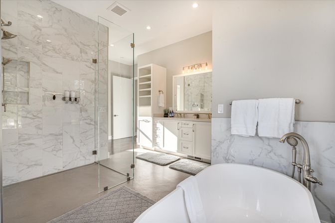 Bright spa-like master bathroom with freestanding soaking tub, chrome fixtures, glass-enclosed marble walk-in shower and white double vanity
