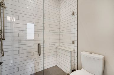 Sleek modern bathroom with a frameless glass walk-in shower clad in white horizontal subway tile, a built-in corner bench, brushed metal fixtures, and an adjacent white toilet.