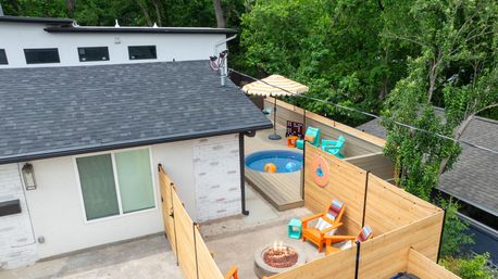 Cozy residential backyard deck with wooden privacy fence, small round plunge pool, striped umbrella, bright Adirondack chairs and a glowing fire pit.