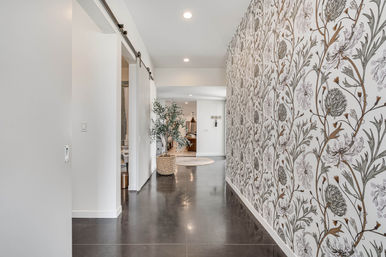 Modern home hallway with a bold botanical floral wallpaper feature wall, dark polished floor, sliding barn door, woven basket planter with potted olive tree and recessed ceiling lights