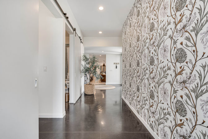 Modern home hallway with a bold botanical floral wallpaper feature wall, dark polished floor, sliding barn door, woven basket planter with potted olive tree and recessed ceiling lights