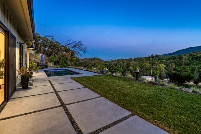 Hilltop backyard patio with concrete pavers, plunge pool, manicured lawn and rolling hills under a twilight sky