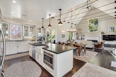 Bright open-concept modern farmhouse kitchen and living room with vaulted white ceiling, large island with farmhouse sink, pendant lights, dining table and dark hardwood floors.