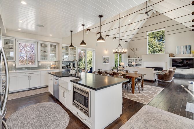 Bright open-concept modern farmhouse kitchen and living room with vaulted white ceiling, large island with farmhouse sink, pendant lights, dining table and dark hardwood floors.