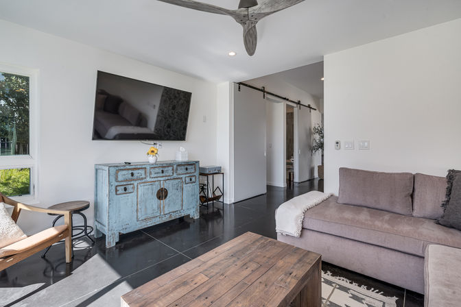 Sunlit modern living room with wall-mounted flat-screen TV above a distressed blue sideboard, gray sectional sofa, rustic wood coffee table, and sliding barn door
