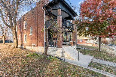 Charming two-story red brick house with covered front porch, stone steps and autumn leaves in a quiet residential neighborhood