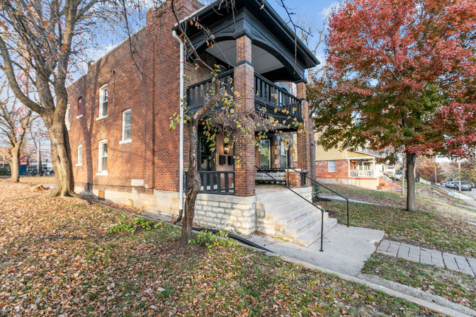 Charming two-story red brick house with covered front porch, stone steps and autumn leaves in a quiet residential neighborhood