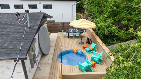 Cheerful residential rooftop deck with a small round plunge pool, turquoise lounge chairs and orange accents, a yellow-striped patio umbrella shading an outdoor dining table, string lights and surrounding trees.