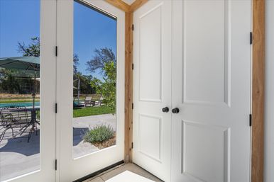Bright entryway with white paneled doors and glass French doors opening onto a sunny backyard patio with pool, lounge chairs, umbrella and metal dining set