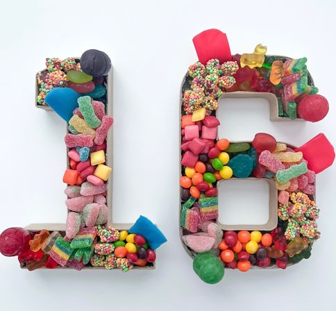 Sweet 16 candy display — numbers 1 and 6 filled with colorful gummy bears, sour strips, jelly beans, chocolate candies and sprinkle clusters on a white background.