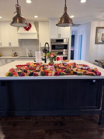 Vibrant charcuterie and floral grazing board spread across a marble kitchen island in a modern white home kitchen under brass pendant lights