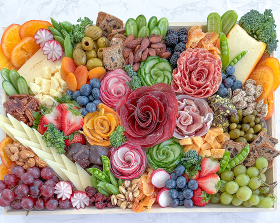 Vibrant artisanal charcuterie board on a wooden tray with rose-shaped cured meats, assorted cheeses, grapes, berries, olives, nuts, dried fruit, crackers and fresh veggies