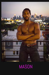 Shirtless athletic man in jeans and layered necklaces standing on a rooftop balcony at dusk, arms crossed with a blurred city skyline and bokeh evening lights in the background.