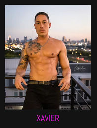 Shirtless muscular tattooed man leaning on an urban rooftop railing at dusk with a blurred city skyline and twinkling lights in the background