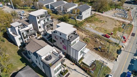 Drone aerial view of sleek multi-story townhouses with rooftop decks, driveways and an adjacent construction lot in a suburban housing development