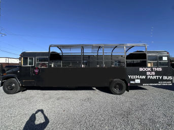 Long black open-sided party bus with metal framing and rooftop rails parked on gravel under a clear blue sky