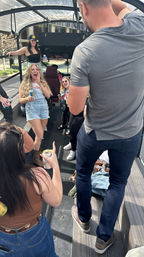 Friends laughing and holding drinks on an open-air party bus cruising a sunny downtown street