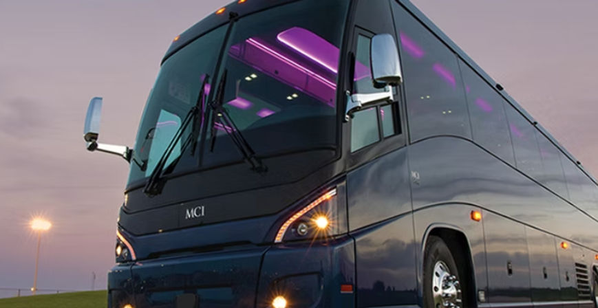 Sleek dark-blue coach bus at dusk with purple interior LED lights, headlights on and chrome side mirrors reflecting the twilight sky.