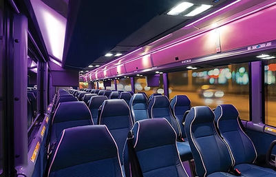 Modern coach bus interior at night with purple LED lighting, blue reclining seats, aisle view, overhead luggage racks and blurred city lights outside
