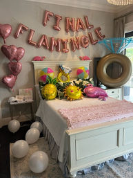 Bedroom bachelorette setup with rose-gold "FINAL FLAMINGLE" balloon banner, heart balloons, tropical inflatables (pineapple, sun, flamingo, oversized diamond ring), beach balls and pink throw on a white bed.