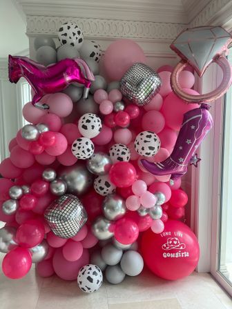 Bright pink and silver indoor balloon wall party backdrop with cow-print and metallic balloons, mirrored disco cubes, pink foil horse, cowboy boot and diamond ring balloons for a cowgirl-themed celebration