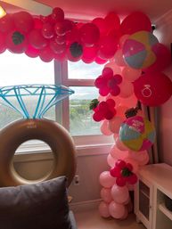 Playful pink balloon garland and flower clusters framing an ocean-view window, with a large inflatable diamond-ring float and colorful beach-ball balloons for a bridal shower celebration.