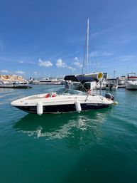 White-and-navy motorboat moored in a sunny coastal marina with turquoise water, yachts and waterfront buildings under a clear blue sky