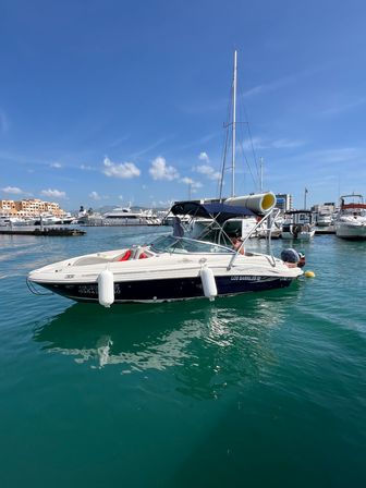 White-and-navy motorboat moored in a sunny coastal marina with turquoise water, yachts and waterfront buildings under a clear blue sky
