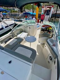Sunny coastal motorboat cockpit with gray cushioned seating, small round table and helm, docked at a busy marina pier