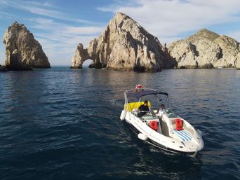 White speedboat cruising near the iconic El Arco rock formations at Cabo San Lucas, Mexico, with deep blue sea and a sunny sky