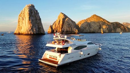 White luxury yacht cruising near towering sunlit sea stacks at golden hour off Cabo San Lucas, Mexico — calm blue waters and warm coastal sunset atmosphere.