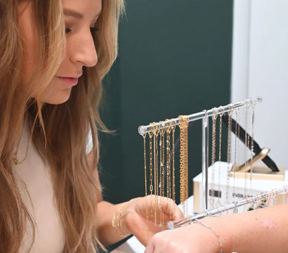 Close-up of a woman trying on delicate gold and silver bracelets from a tabletop jewelry rack in a boutique