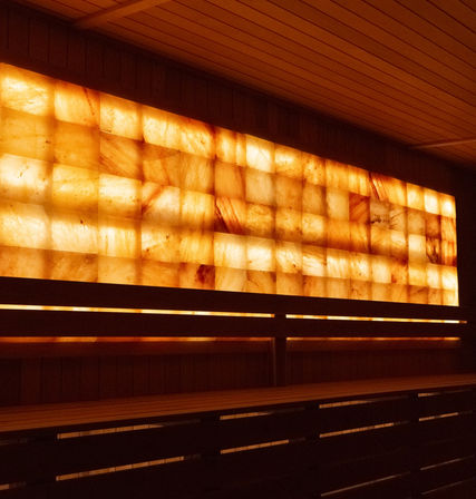 Backlit Himalayan salt brick wall glowing amber behind wooden sauna benches in a cozy spa setting