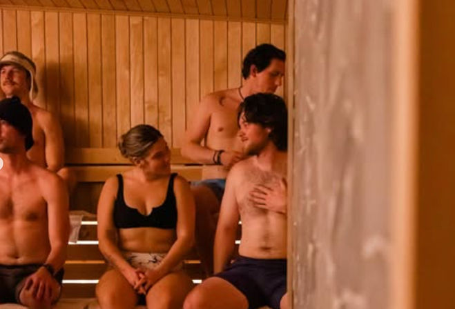 Group of adults in swimwear chatting and relaxing on wooden benches inside a warm indoor sauna at a spa or wellness center