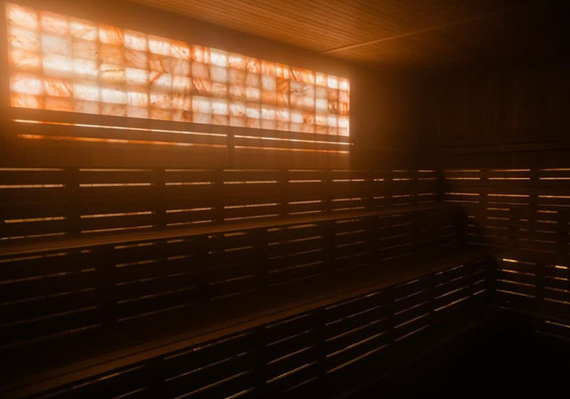 Amber-lit indoor sauna with tiered wooden benches and a glowing backlit salt wall, warm hazy atmosphere