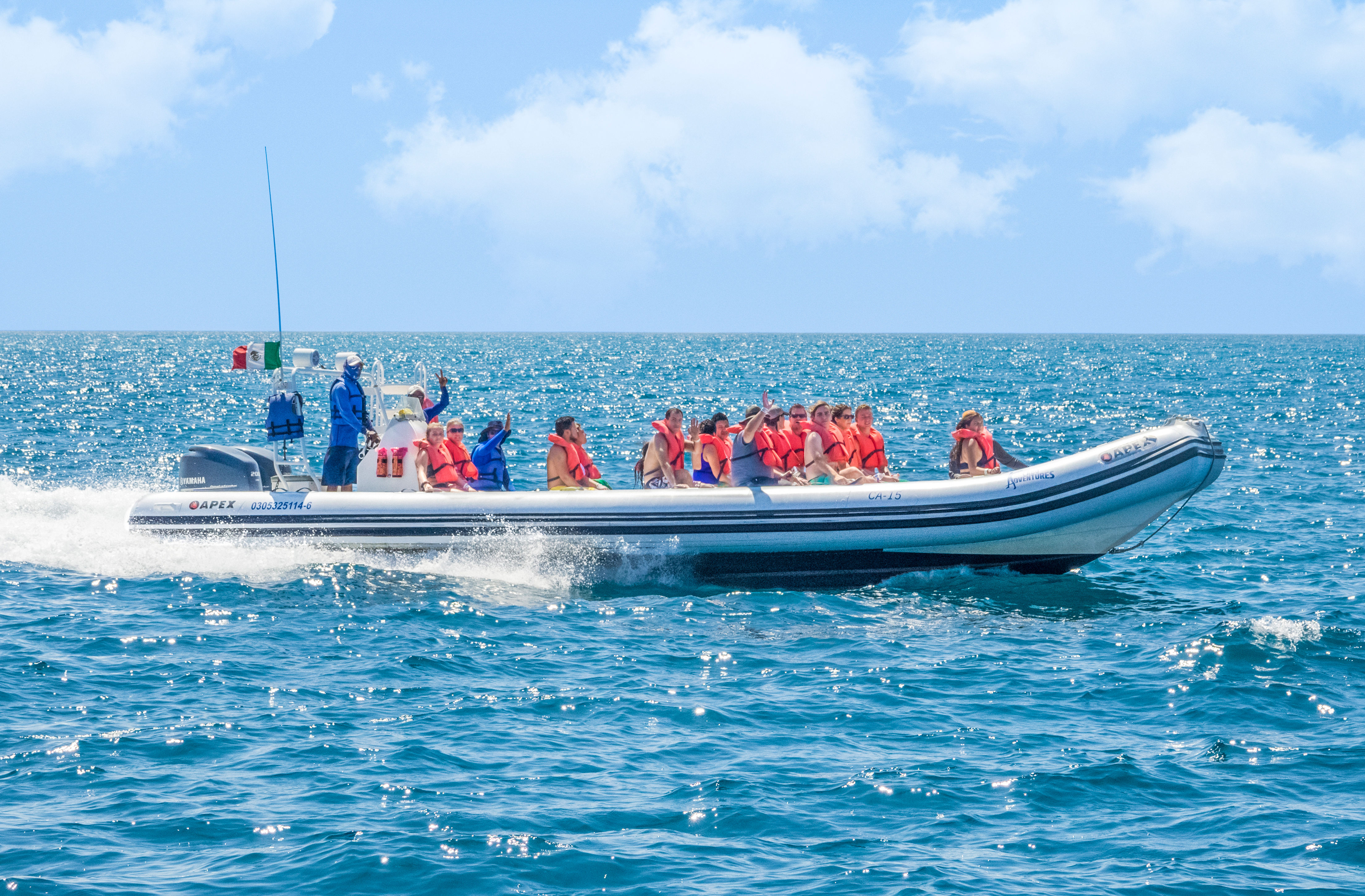 Group of passengers in orange life jackets on a white inflatable speedboat speeding across sparkling turquoise ocean on a sunny day — ocean tour vibe.