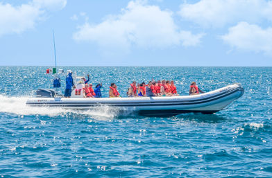 Group of passengers in orange life jackets on a white inflatable speedboat speeding across sparkling turquoise ocean on a sunny day — ocean tour vibe.