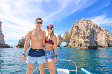 Couple on a boat enjoying a sunny vacation by a dramatic coastal sea arch and sunlit limestone cliffs over turquoise water