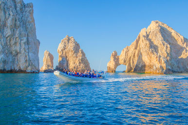 Speedboat of passengers in life vests speeding past the iconic El Arco limestone rock formations at Land's End, Cabo San Lucas, Mexico, with sparkling blue water and a clear sky