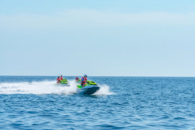 Three riders on bright green jet skis speeding across open blue ocean, spraying white wake.