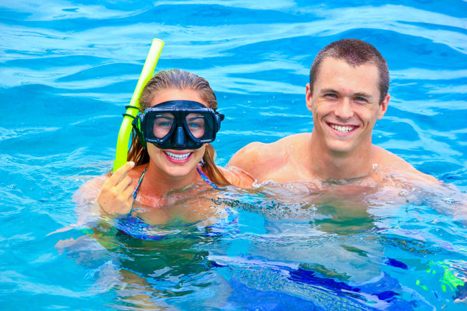 Smiling couple snorkeling in clear turquoise water, woman wearing a black mask and yellow snorkel and a man swimming beside her