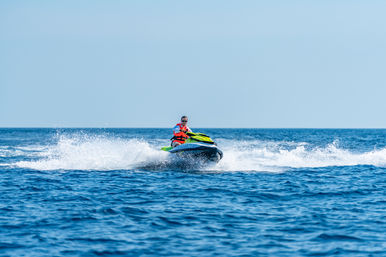 Person on a bright green and yellow jet ski speeding across deep blue ocean, kicking up white spray and waves under a clear sky