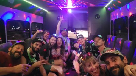 Smiling group of friends posing for a selfie inside a disco-lit party bus at night, colorful LED and laser lights reflecting on seats and windows.