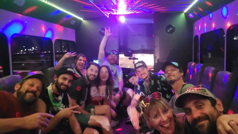 Smiling group of friends posing for a selfie inside a disco-lit party bus at night, colorful LED and laser lights reflecting on seats and windows.