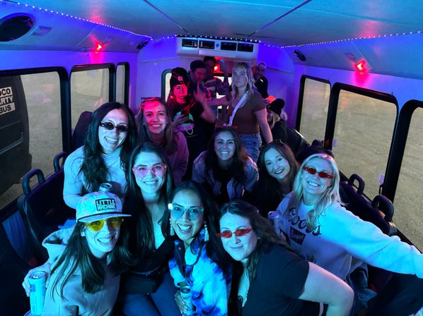 Cheerful group of friends inside a LED-lit party shuttle, wearing colorful sunglasses and casual outfits, smiling and holding drinks