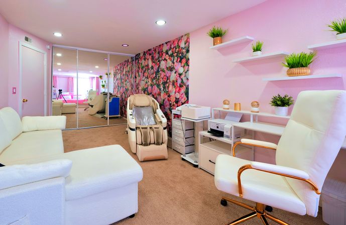 Cozy pink salon room with floral accent wall and mirrored closet doors, beige massage recliner, white office and sectional seating, and floating shelves with potted plants.