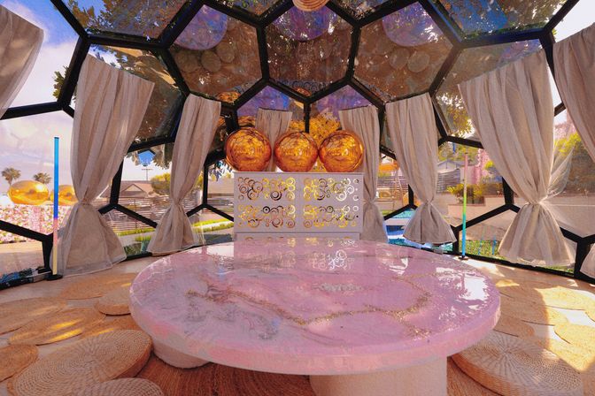 Sunlit geodesic dome backyard lounge with a glossy pink marble round table, woven floor cushions, beige tie-back curtains, decorative cabinet topped with three reflective gold spheres, and garden and pool views.