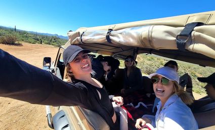 Smiling friends taking a sunny selfie from an open-top jeep driving through a saguaro-studded Sonoran Desert landscape