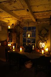 Candlelit rustic attic workspace at night with exposed wooden beams, a vintage typewriter on a draped table surrounded by small pumpkins, flameless candles, an antique mirror and brass instrument by a multi-pane window.