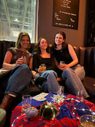 Three friends in jeans enjoying cocktails on a cozy booth in an indoor lounge with festive table decor